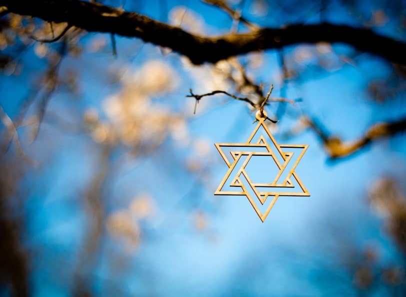 Wooden Star of David ornament hanging from a tree branch with a blue sky background.