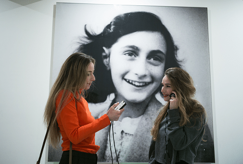 Two women using audio guides in front of Anne Frank portrait.