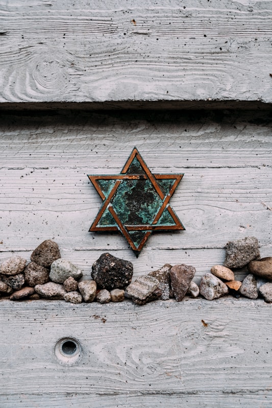 Rustic Star of David mounted on wood with memorial stones placed below.