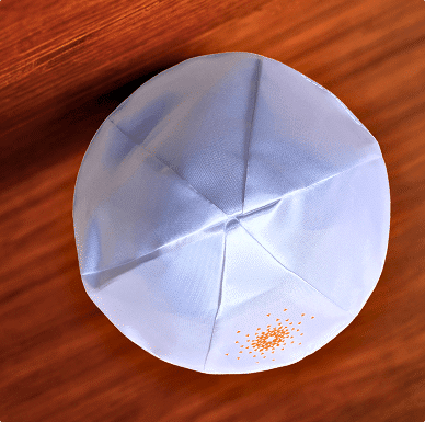 White kippah (yarmulke) with orange embroidery on a wooden surface.