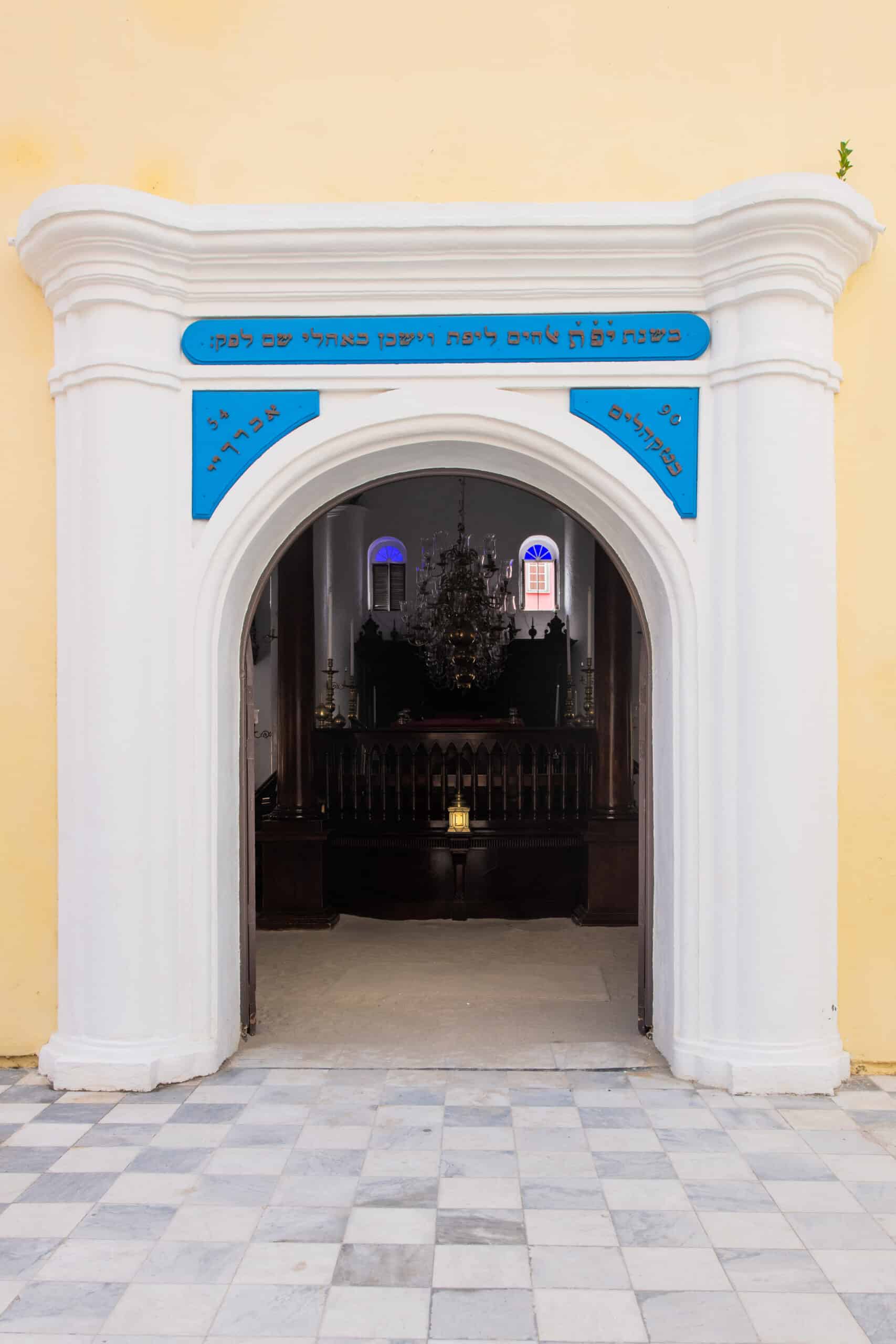 Ornate entrance to the historic synagogue in Curaçao, featuring Hebrew inscriptions and leading to the main sanctuary of the Jewish Museum.