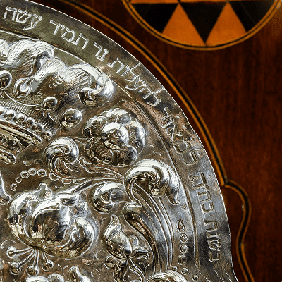Close-up of embossed Hebrew text and decorative elements on silver plate.
