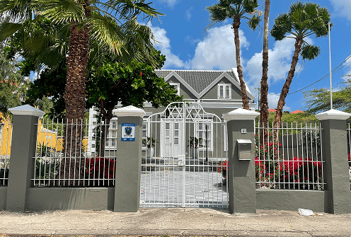 Historic house behind a white metal gate with palm trees in Curaçao.