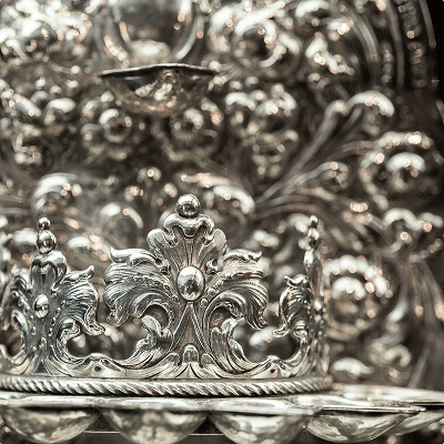 Silver crown ornament with intricate floral details on ceremonial background.