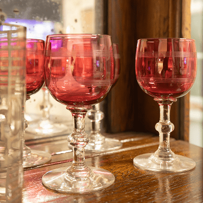 Vintage red wine glasses reflected in a mirror on a wooden surface.
